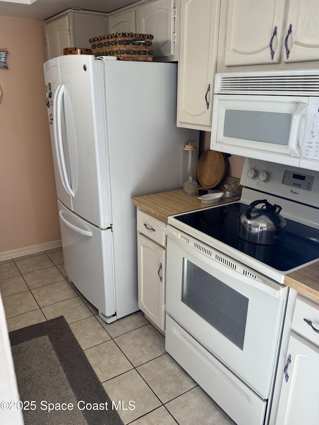 kitchen featuring white appliances, light tile patterned floors, and white cabinets