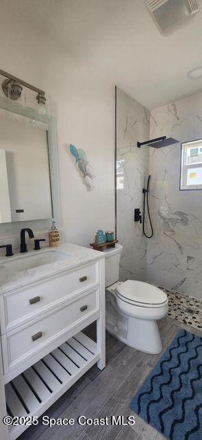 bathroom with hardwood / wood-style flooring, toilet, vanity, and tiled shower