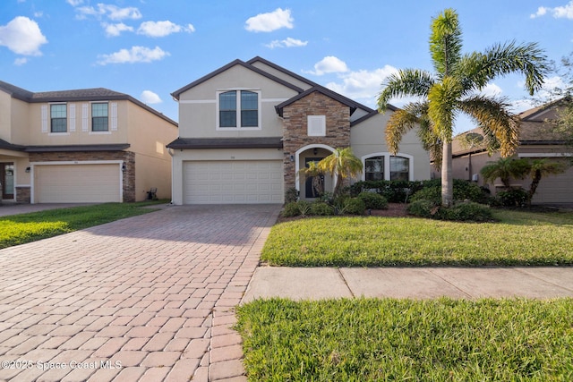 traditional-style home featuring decorative driveway, stucco siding, a front yard, a garage, and stone siding