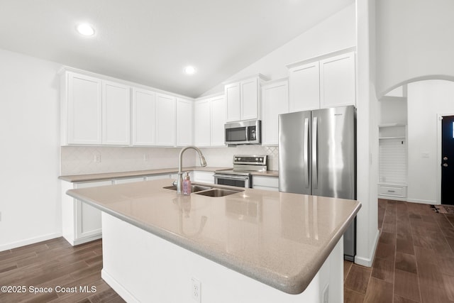 kitchen featuring a center island with sink, light stone counters, stainless steel appliances, white cabinetry, and a sink