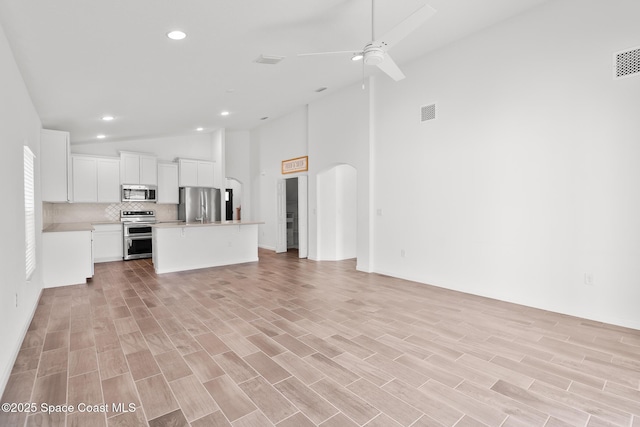 unfurnished living room featuring arched walkways, ceiling fan, high vaulted ceiling, visible vents, and light wood finished floors