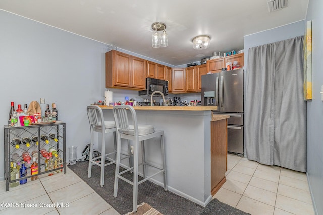 kitchen featuring stainless steel refrigerator with ice dispenser, light tile patterned flooring, a breakfast bar, sink, and kitchen peninsula