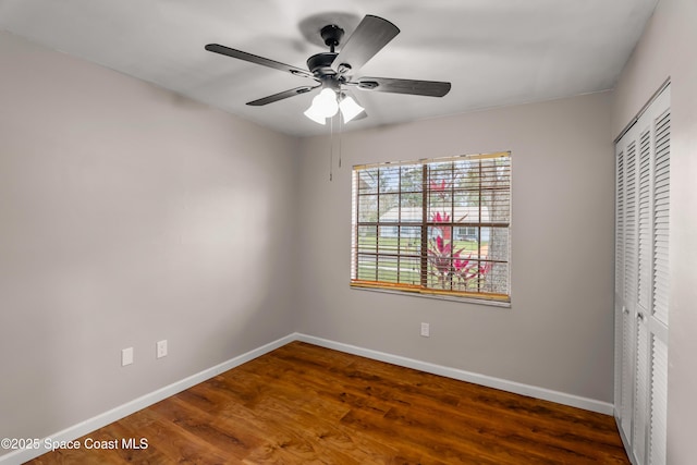 unfurnished bedroom with dark wood-style floors, a closet, baseboards, and a ceiling fan