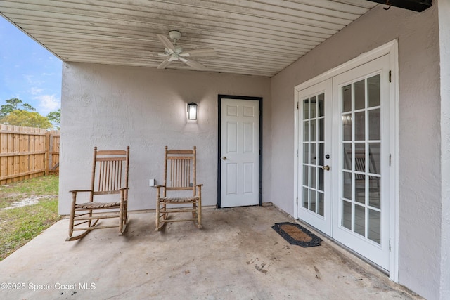 view of exterior entry featuring french doors, stucco siding, a patio area, ceiling fan, and fence