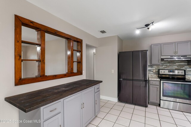 kitchen featuring under cabinet range hood, visible vents, stainless steel range with electric cooktop, freestanding refrigerator, and decorative backsplash