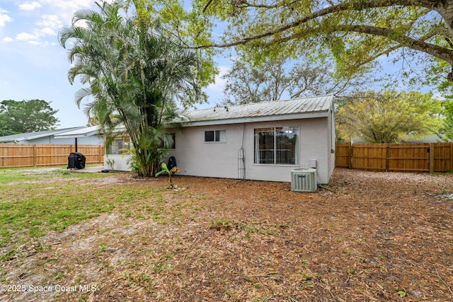 back of house featuring metal roof, central AC, a fenced backyard, and stucco siding