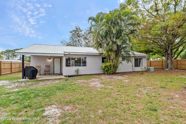 rear view of house with central air condition unit, a fenced backyard, a lawn, and stucco siding