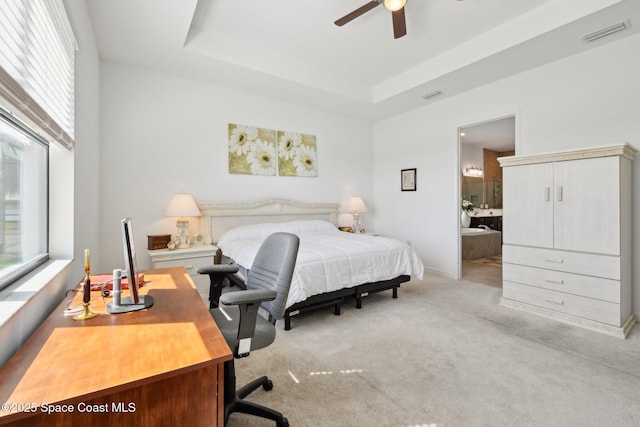 bedroom with light carpet, visible vents, a tray ceiling, and a ceiling fan