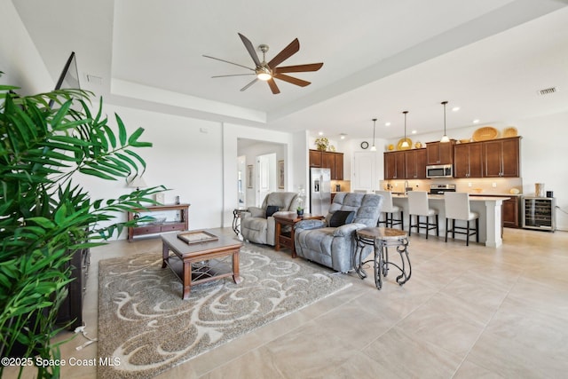 living area with a tray ceiling, wine cooler, recessed lighting, visible vents, and a ceiling fan