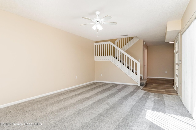carpeted empty room with stairway, ceiling fan, and baseboards