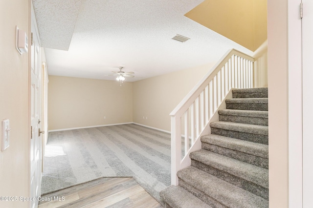 stairs featuring a ceiling fan, visible vents, baseboards, a textured ceiling, and wood finished floors