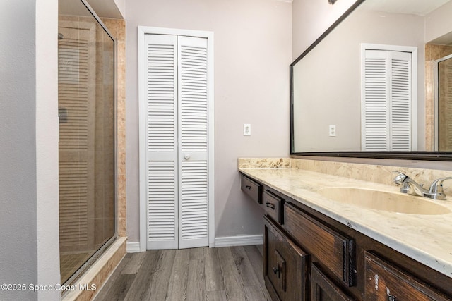 full bathroom with wood finished floors, a shower stall, a closet, vanity, and baseboards