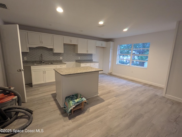 kitchen with sink, light stone counters, a kitchen island, white cabinets, and decorative backsplash