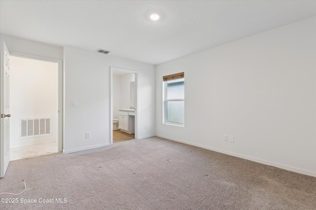 unfurnished bedroom with baseboards, visible vents, ensuite bathroom, and light colored carpet