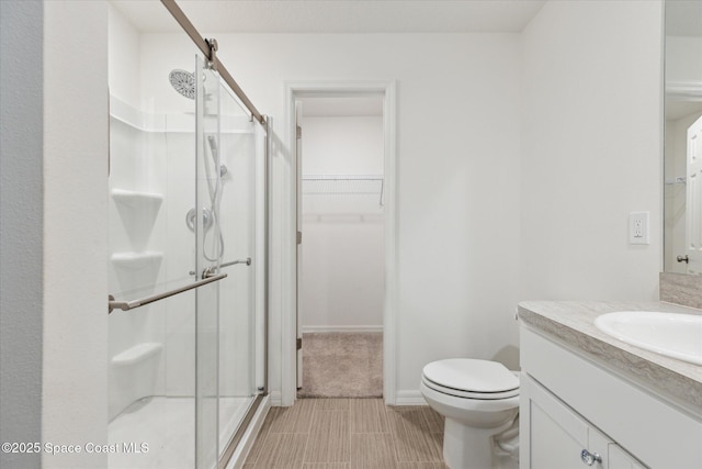 bathroom featuring baseboards, toilet, a spacious closet, vanity, and a shower stall