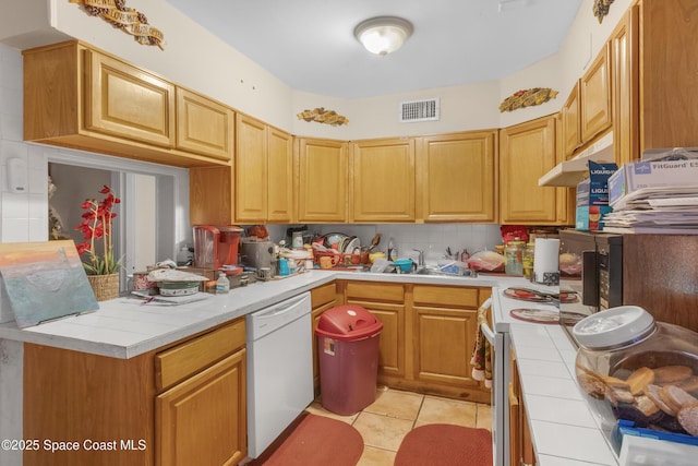 kitchen with tile counters, light tile patterned floors, decorative backsplash, and dishwasher