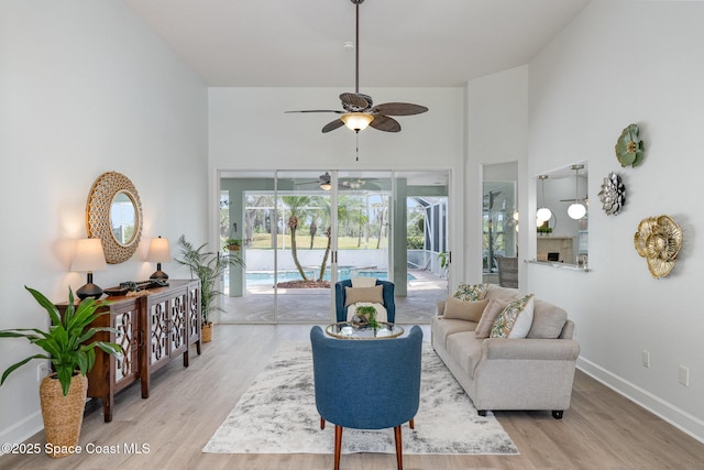 living room with a fireplace, a towering ceiling, light wood-style flooring, a sunroom, and baseboards