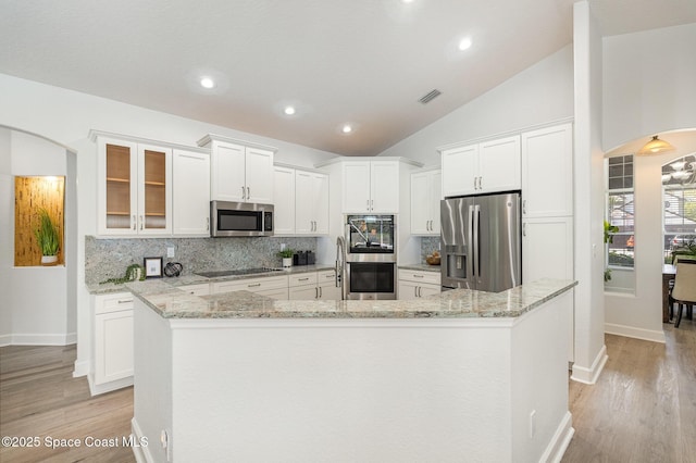 kitchen featuring white cabinets, arched walkways, stainless steel appliances, and decorative backsplash