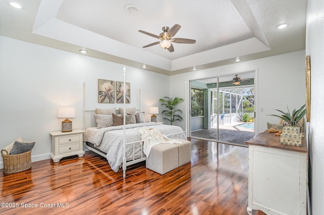 bedroom featuring access to exterior, a raised ceiling, wood finished floors, and a sunroom