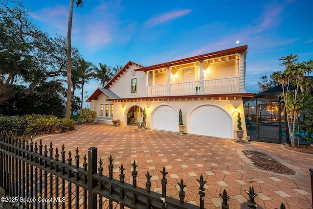 mediterranean / spanish-style home featuring a fenced front yard, a balcony, a garage, and stucco siding