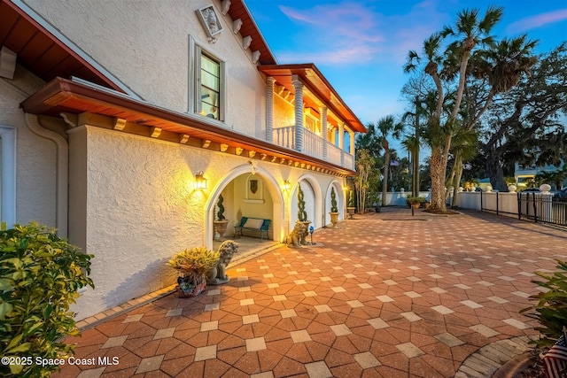 back of house at dusk featuring a patio area, fence, a balcony, and stucco siding