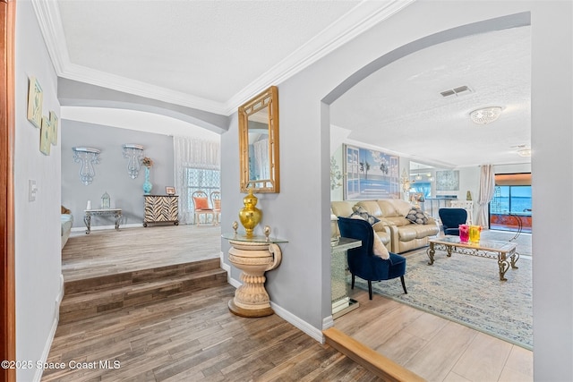 hallway with ornamental molding, arched walkways, visible vents, and wood finished floors