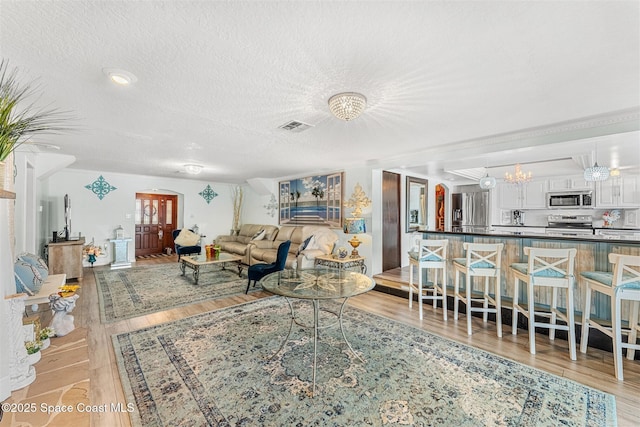 living area featuring arched walkways, a notable chandelier, visible vents, light wood-style flooring, and a textured ceiling