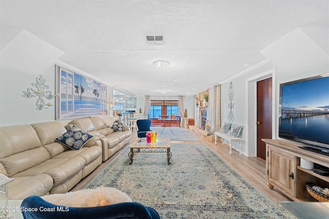 living area with light wood-type flooring, visible vents, a textured ceiling, and ornamental molding