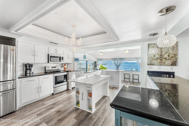 kitchen with white cabinets, a raised ceiling, a kitchen island, appliances with stainless steel finishes, and pendant lighting