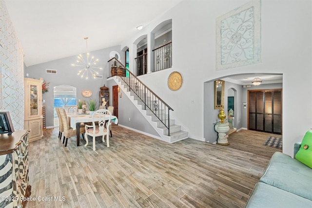 dining space with arched walkways, a notable chandelier, stairway, and wood finished floors