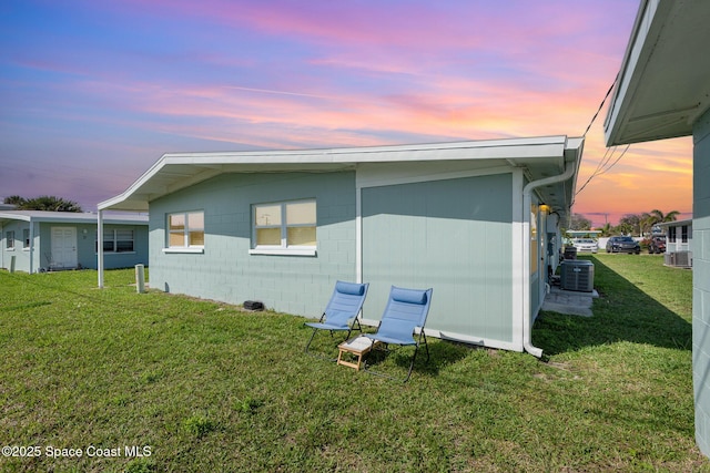 view of side of property featuring central AC unit, concrete block siding, and a yard