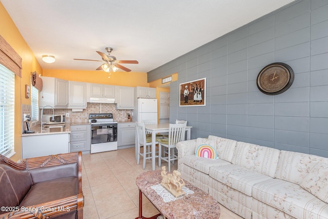 living area with ceiling fan, light tile patterned flooring, and tile walls