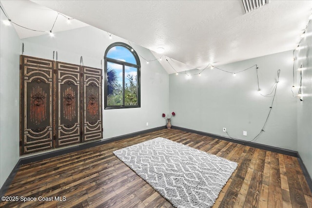 interior space featuring dark wood-style floors, vaulted ceiling, a textured ceiling, and baseboards