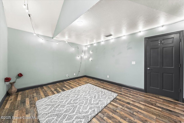 spare room with dark wood-style flooring, visible vents, a textured ceiling, and baseboards