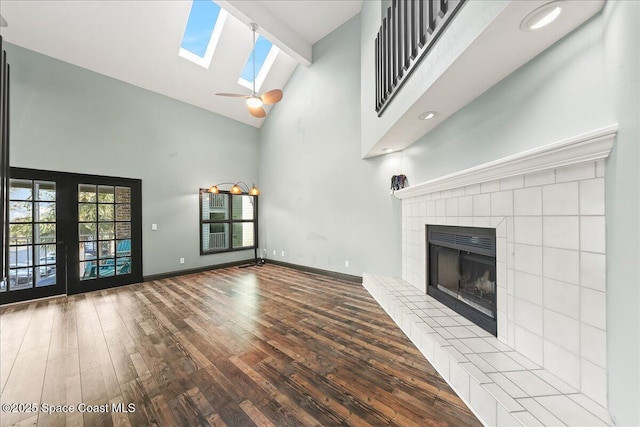 unfurnished living room featuring a skylight, baseboards, a tile fireplace, wood finished floors, and high vaulted ceiling