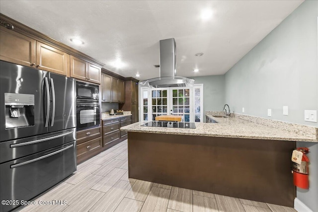 kitchen featuring light stone countertops, island range hood, a sink, wood tiled floor, and black appliances