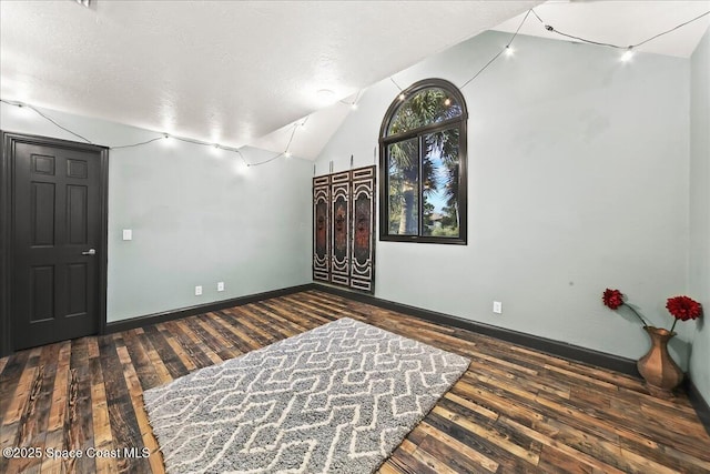 empty room with lofted ceiling, dark wood-style flooring, a textured ceiling, and baseboards