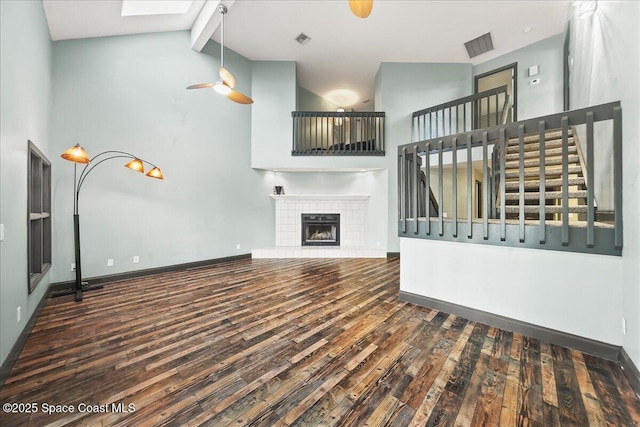 unfurnished living room featuring high vaulted ceiling, dark wood-style flooring, baseboards, beamed ceiling, and a tiled fireplace