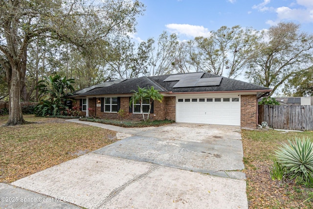 ranch-style house featuring concrete driveway, an attached garage, fence, roof mounted solar panels, and brick siding