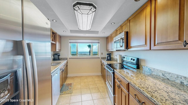 kitchen featuring light tile patterned floors, appliances with stainless steel finishes, brown cabinetry, and light stone counters