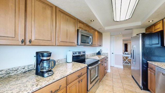 kitchen with light tile patterned flooring, recessed lighting, appliances with stainless steel finishes, light stone countertops, and a tray ceiling