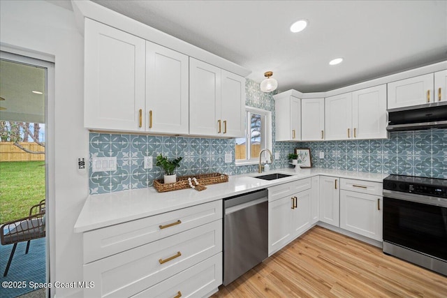 kitchen with stainless steel appliances, light countertops, white cabinets, a sink, and under cabinet range hood