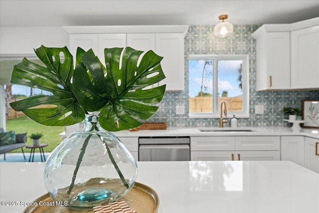 kitchen featuring stainless steel dishwasher, white cabinetry, light countertops, and a sink