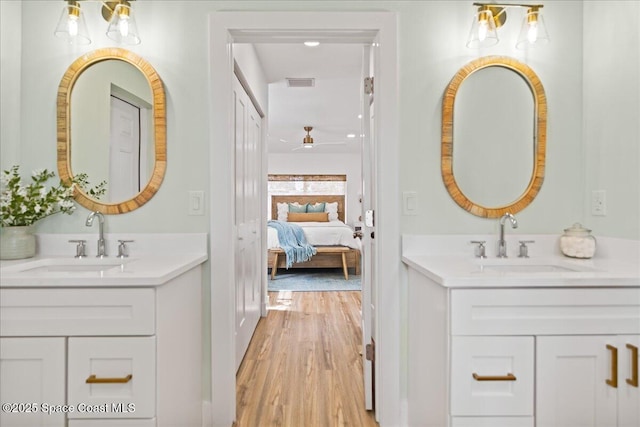 ensuite bathroom featuring visible vents, a sink, ensuite bath, and wood finished floors