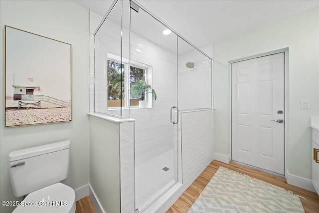 bathroom with toilet, a stall shower, baseboards, and wood finished floors