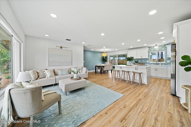 living room with recessed lighting, baseboards, visible vents, and light wood finished floors