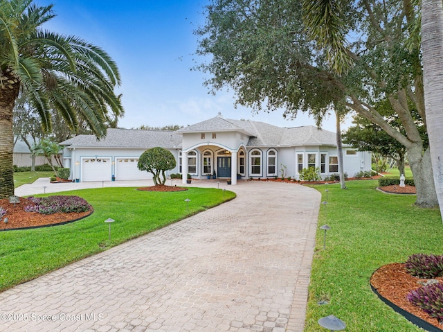 view of front facade featuring an attached garage, stucco siding, decorative driveway, and a front yard