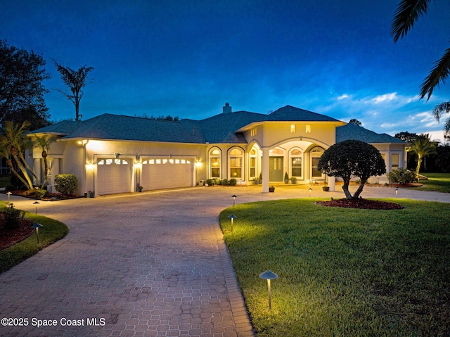 mediterranean / spanish home with a garage, stucco siding, curved driveway, and a front yard