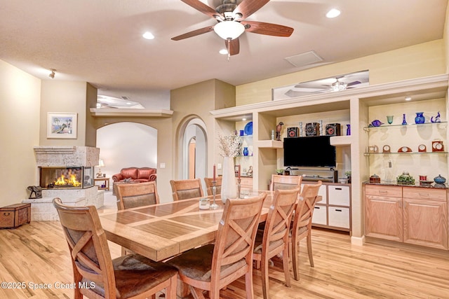 dining space with light wood-type flooring, ceiling fan, arched walkways, and a high end fireplace