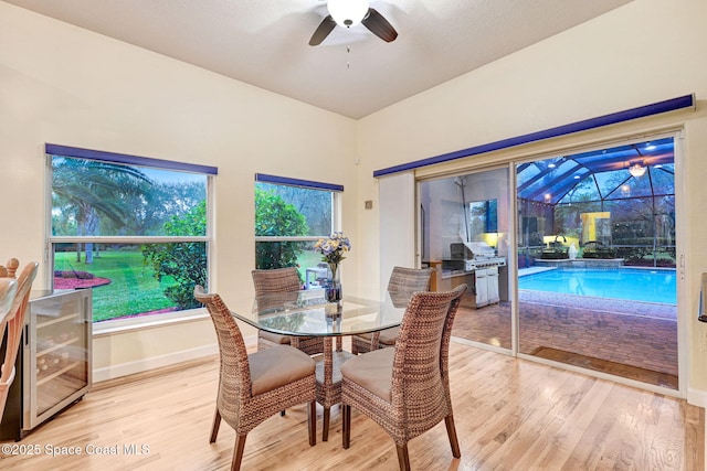 dining room with a sunroom, ceiling fan, wood finished floors, beverage cooler, and baseboards